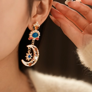 Close-up of vintage gold moon and star earrings with colorful gems and pearls on model