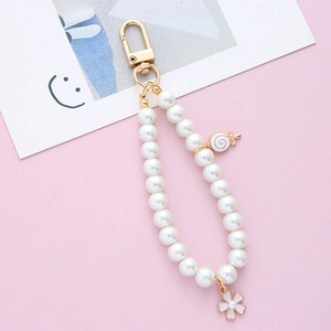 Close-up of pearl keychain with white lollipop and flower charms on pink background