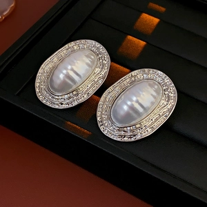 Close-up of vintage silver oval earrings with textured white pearl inlays and metal embossing