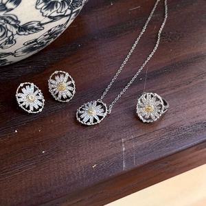 Macro shot of silver daisy jewelry set with necklace, earrings and ring on dark wood