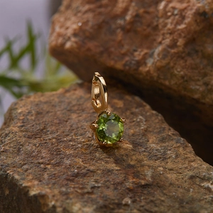 Macro shot of gold-plated S925 silver charm with round-cut green gemstone on stone