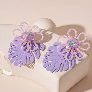 Detail of lavender beaded flower earrings with hollow monstera leaf on stone display