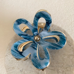 Detail view of acetate flower hair claw with blue marble texture and gold metal edging