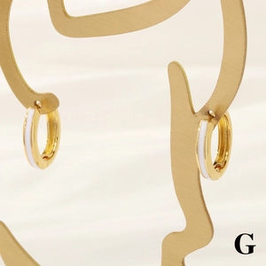 Detail of 18K gold plated hoop earrings with white enamel on a gold artistic stand
