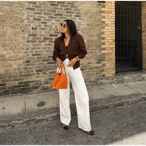 Detail of orange leather bucket bag styled with a V-neck knit cardigan and white trousers