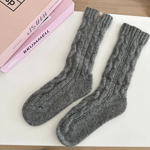 Detailed macro view of grey cable-knit wool socks featuring a small round fabric label