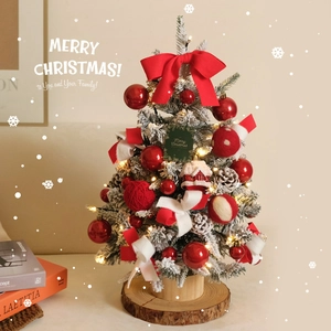 Mini snowy Christmas tree with red bows and warm LED lights on a rustic wooden base