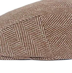 Detailed close-up of brown herringbone tweed fabric with precise stitching on newsboy cap
