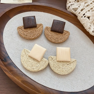Detail of bohemian raffia woven earrings with square wood studs on linen fabric