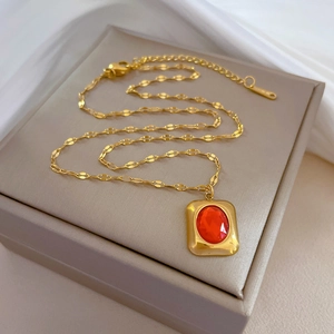 Detail of vintage gold necklace with rectangular pendant and red gemstone on a jewelry box
