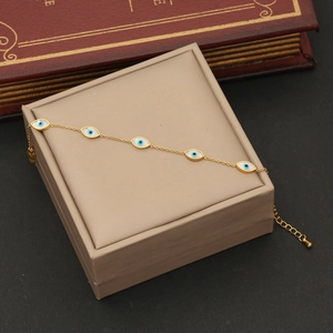 Gold evil eye bracelet with white oval beads and blue eye motifs on jewelry box