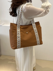 Dettaglio di una borsa tote in nylon marrone con ampie tracolle a motivi geometrici colorati