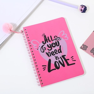 Detalle de cuaderno de espiral rosa con pompón de peluche y diseño All You Need Is Love
