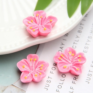 Macro shot of three pink resin cherry blossom charms with yellow stamens on ceramic plate