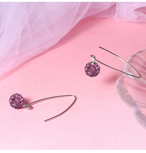 Macro view of purple pavé crystal ball earrings with silver hooks on a pink background