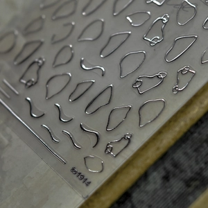 Macro shot of silver laser nail stickers with irregular metallic foil patterns and shapes