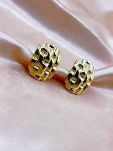Detail of gold woven texture earrings on pink silk background with soft lighting
