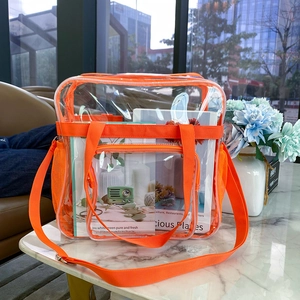 Detail der transparenten PVC-Schultertasche mit orangefarbenem Rand auf Marmortisch