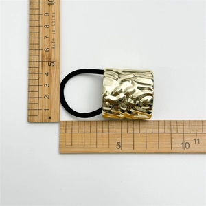 Detail shot of golden metal hair tie with irregular texture showing 3.5cm size scale
