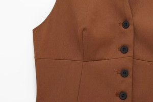 Détail du tissu en sergé marron d'un gilet avec bouton noir et coutures de qualité
