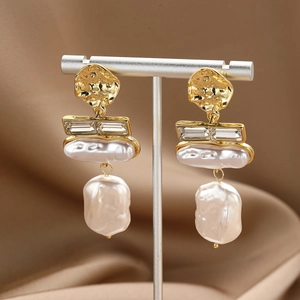 Detailed view of long baroque pearl earrings with sparkling crystals on a golden display