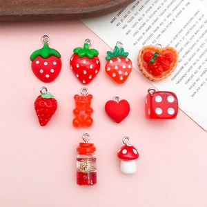 Close-up of red resin charms including strawberry mushroom and heart on pink background