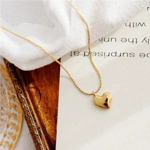 Polished gold heart pendant necklace on minimalist chain over textured fabric background