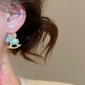 Macro shot of a pearl earring with light blue enamel rocking horse pendant and gold metal trim