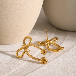 Detailed close-up of golden bow earrings with heart pendants on a textured stone surface