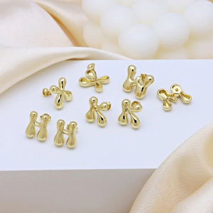 Polished gold bubble letter earrings H K M W displayed on luxury champagne silk fabric
