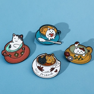 Flat lay of four colorful cartoon cat coffee cup enamel pins on a blue textured surface