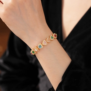 Detail of model wearing a gold bracelet with multi-colored heart-shaped zircon stones
