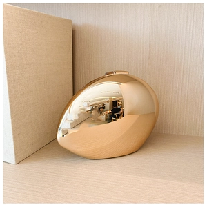 Close-up of golden oval acrylic clutch bag with a high-shine mirror finish and metal clasp