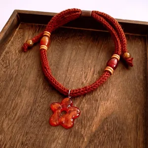 Handcrafted red woven necklace with plush floral pendant and wooden beads on wood tray
