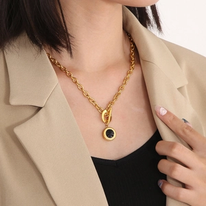 Detail of gold chunky chain necklace with OT buckle and black gemstone pendant on a model