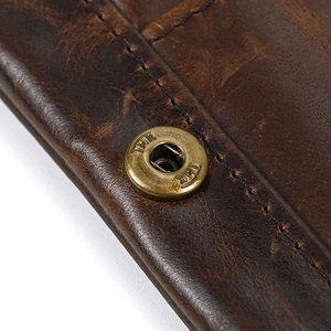 Macro shot of dark brown genuine leather texture with bronze snap button and neat stitching
