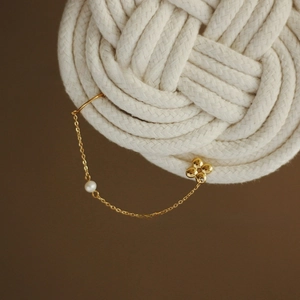 Close-up of golden clover leaf tassel earring with pearl accent on woven background