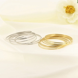 Minimalist multi-layered stainless steel bangles in gold and silver finish on white fabric