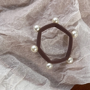 Detailed view of a brown elastic hair tie featuring six glossy white pearls on a soft base