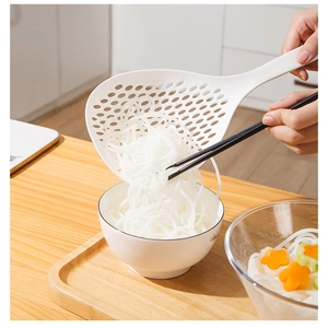 Close-up of white plastic slotted spoon scooping noodles in a bright kitchen