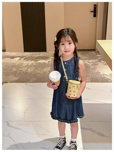 Girl in denim dress wearing a beige cherry bucket bag while holding a cup of coffee