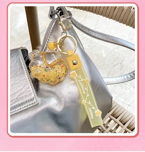 Close-up of yellow shell keychain with floating star sequins on a silver handbag