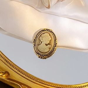 Detailed close-up of retro relief cameo brooch with gold floral frame on silk