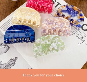 Flat lay of six acetate hair claws in various marble colors on a stylish magazine