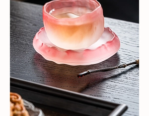 Detailed close-up of pink gradient frosted glass tea cup and saucer on dark wooden table
