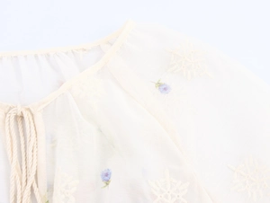Détail d'une blouse française avec broderie florale et cordons de serrage à glands