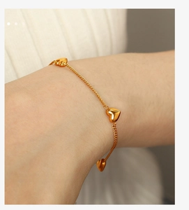 Detail of gold heart pendant bracelet with multiple charms worn on a woman wrist