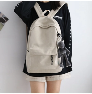 Detail of minimalist cream canvas backpack with a cute plush frog pendant for travel