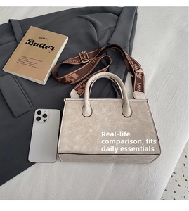 Detail view of cream lychee textured leather tote bag with a brown branded wide shoulder strap