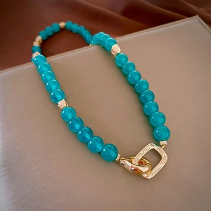 Macro detail of turquoise beads with golden textured interlocking clasp on satin